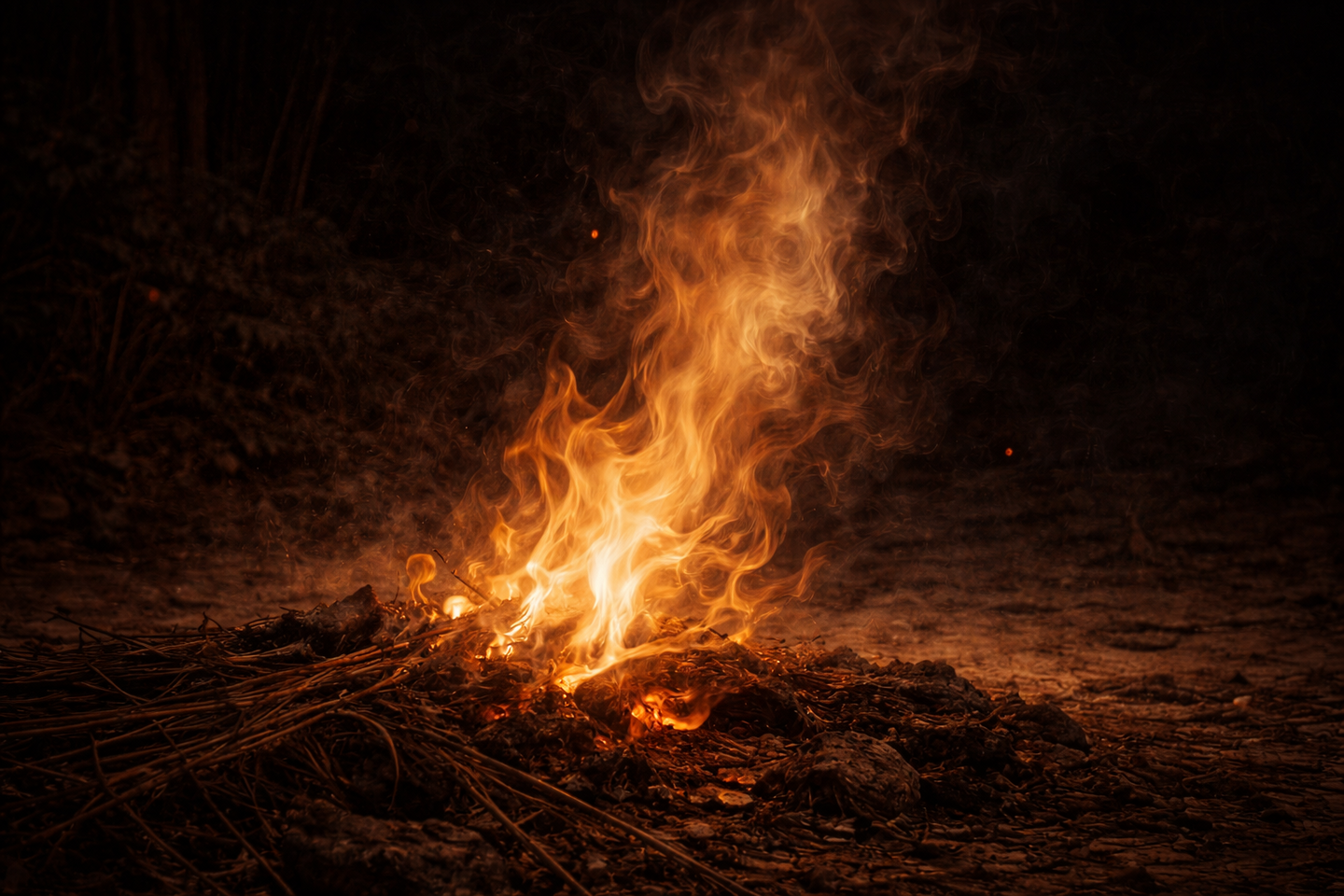 地面に焚かれた小さな火の炎が暗闇の中で揺らめき、火影の中に人の顔のようにも見える陰影が浮かんでいる。周囲には藁や土が見える。